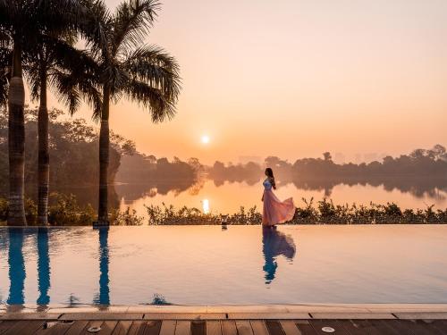 a woman standing on the edge of a pool at sunset at LOTTE Hotel Serviced Apartment in Yangon