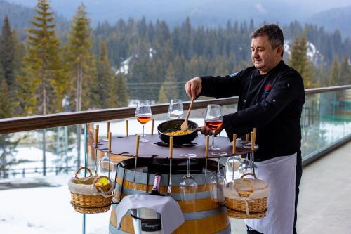 a man standing on a balcony with a table with wine glasses at Hotel Belmont & Spa in Sinaia