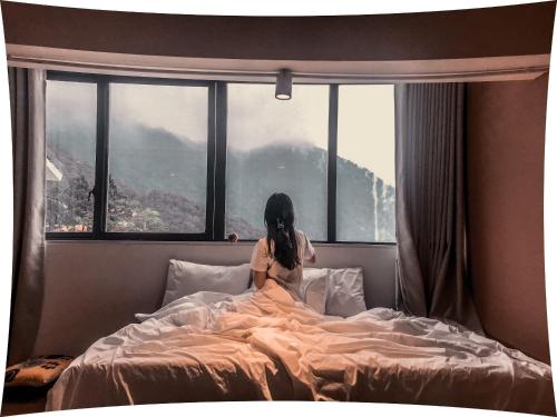 a girl sitting on a bed looking out a window at Le vent Tam Đảo homestay in Tam Ðảo