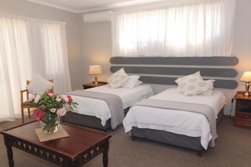 a hotel room with two beds and a table with flowers at The Village Guesthouse in Ceres