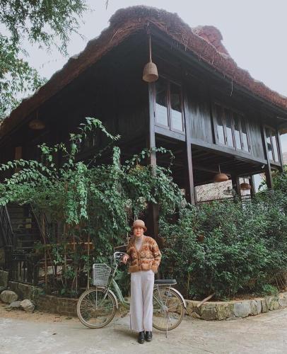 a man standing in front of a house with a bike at Mai Chau Rustic Home in Mai Chau
