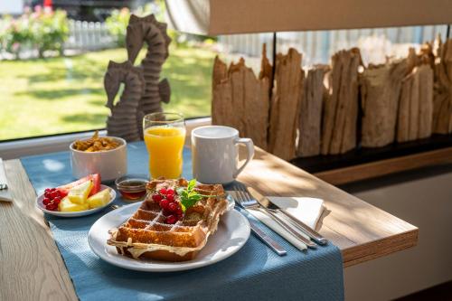 ビューズムにあるDas Frühstückshotel Büsumの- ワッフル、フルーツ、オレンジジュースの朝食をテーブルに用意しています。