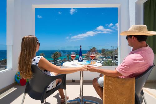 a man and woman sitting at a table with glasses of wine at Apartamentos Galeon Playa in Costa Teguise