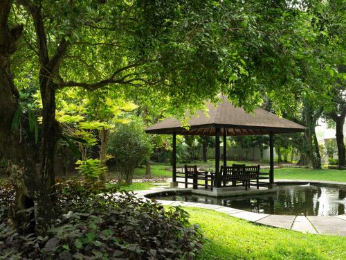 a gazebo with benches and a pond in a park at Royal Ambarrukmo Yogyakarta in Yogyakarta