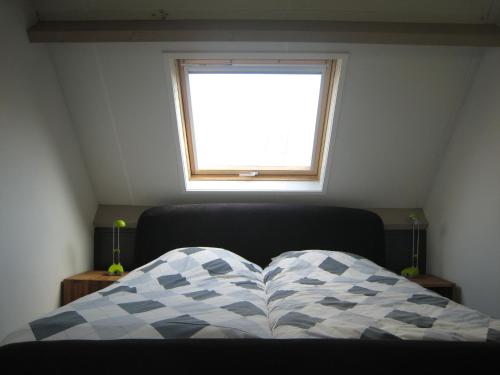 a bed with a checkered blanket and a window at These two holiday homes built in 2006 in Zuidzande