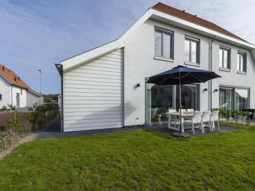 een wit huis met een tafel en een paraplu bij Luxurious villa a 5 minute walk from beach in Cadzand