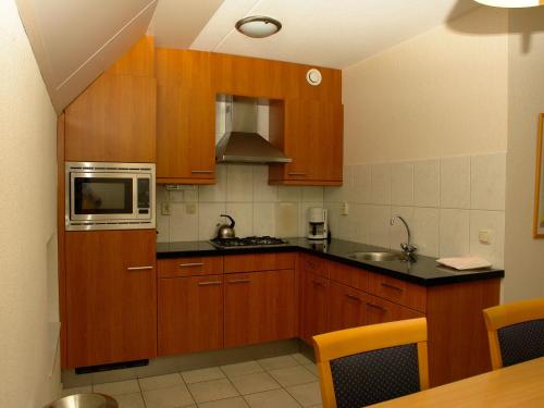 cocina con armarios de madera y microondas en Restful Apartment with Garden, Private Terrace,Swimming Pool, en Westerbork