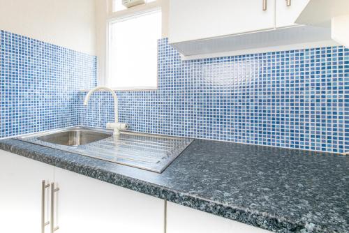 a kitchen with a sink and a blue tiled wall at Sandpiper Holiday Apartments in Blackpool