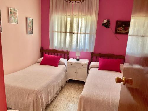 a bedroom with two beds with pink walls and a window at Los Robles in Ávila