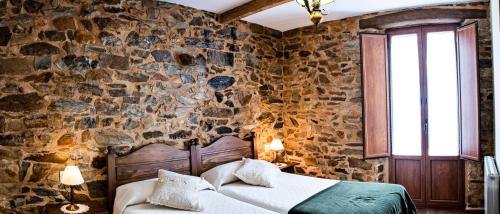 1 dormitorio con pared de piedra, cama y ventana en Casa El Habanero II en Destriana