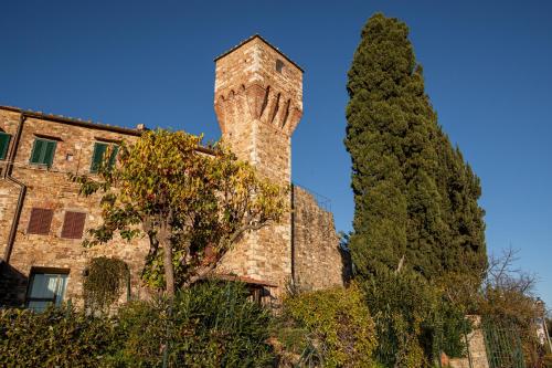 a tall tree next to a building with a tower at old medieval apartment in San Donato in Poggio