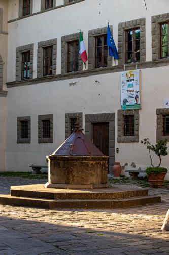 a building with a fountain in front of a building with flags at old medieval apartment in San Donato in Poggio