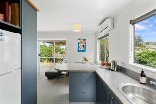 a kitchen with a sink and a table and a window at The Wee Blue Bach - Waikanae Beach Holiday Home in Waikanae