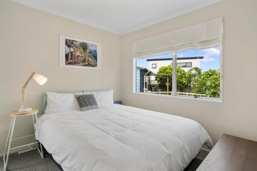 a white bedroom with a bed and a window at The Wee Blue Bach - Waikanae Beach Holiday Home in Waikanae