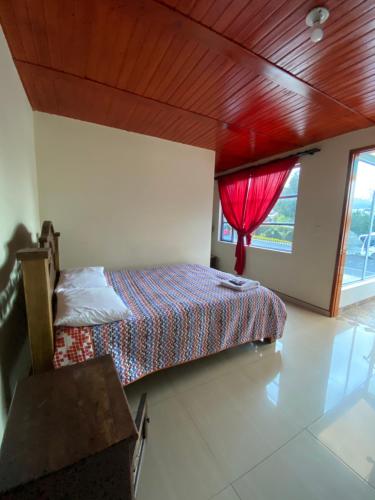 a bedroom with a bed with a red curtain and a window at Hotel Las Palmeras Gachancipa in Gachancipá