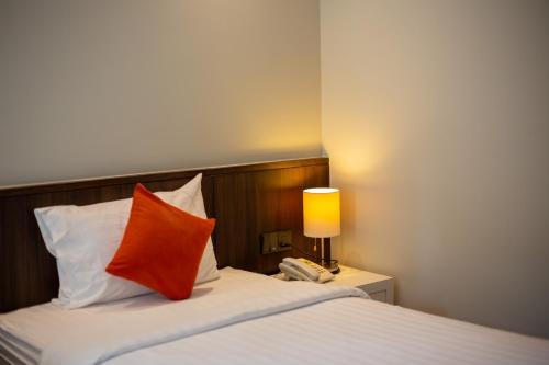 a bedroom with a bed with an orange pillow and a lamp at Lemontea Hotel Bangkok in Bangkok
