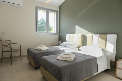 two beds in a bedroom with a chair and a window at Villa Valenza in Favara