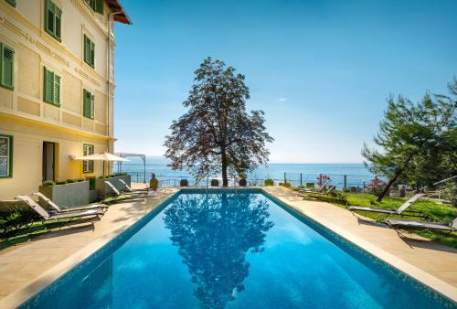 a swimming pool with chairs and the ocean in the background at Apartments Belvedere - by Liburnia Hotels & Villas in Lovran