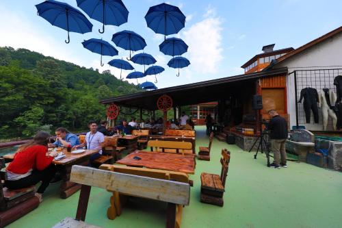 a group of people sitting at tables under blue umbrellas at Dzajicaa Buk Rooms - Noahs Ark in Konjic