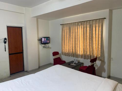 a bedroom with a bed and two chairs and a television at JK Rooms 147 Lions - Koradi Nagpur in Nagpur