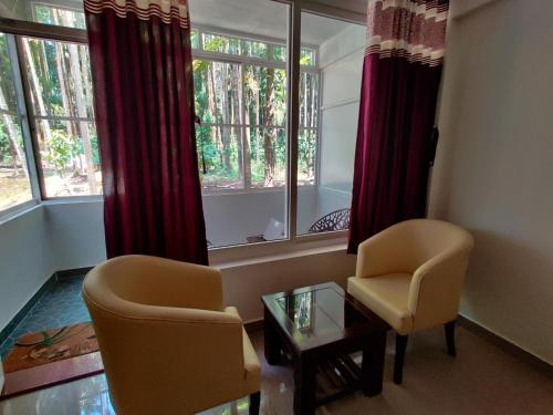 a living room with two chairs and a table and windows at Hosamane Farm Inn in Sringeri