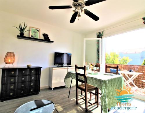 ein Wohnzimmer mit einem Tisch und einem Deckenventilator in der Unterkunft Hyères-plage Studio cabine-L'ayguade BY HC in Hyères