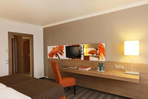 a bedroom with a desk with a television and a bed at SOALTEE Hotel by Trip Inn Frankfurt Messe Tagungshotel in Frankfurt/Main
