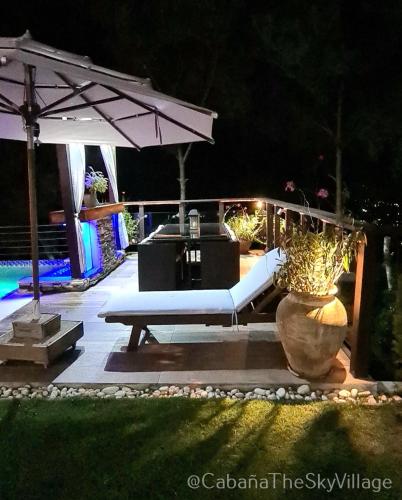 a patio with a bench and an umbrella at night at Villa The sky village in Jarabacoa