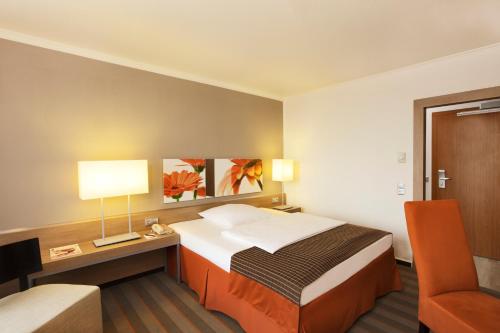 a hotel room with a bed and a desk and a chair at H4 Hotel Frankfurt Messe in Frankfurt/Main