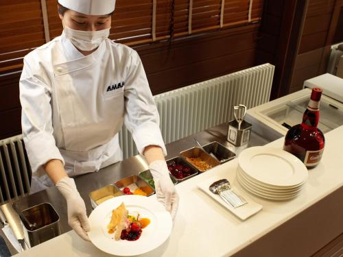 a chef in a kitchen holding a plate of food at Lake Shikotsu Tsuruga Resort Spa Mizu no Uta in Chitose