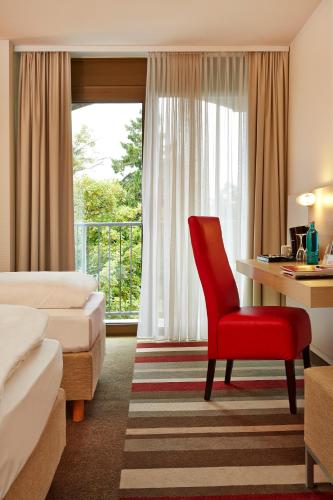 a hotel room with a red chair and a desk at H+ Hotel Bad Soden in Bad Soden am Taunus