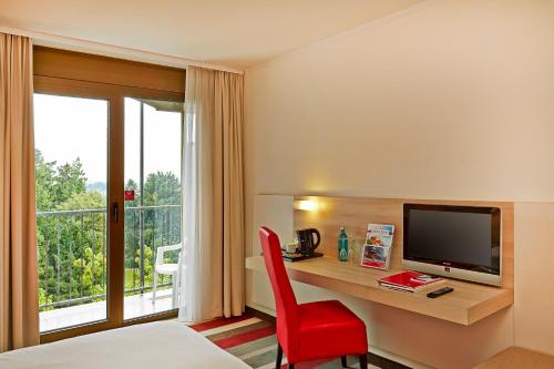 Habitación de hotel con escritorio, TV y silla roja. en H+ Hotel Bad Soden, en Bad Soden am Taunus