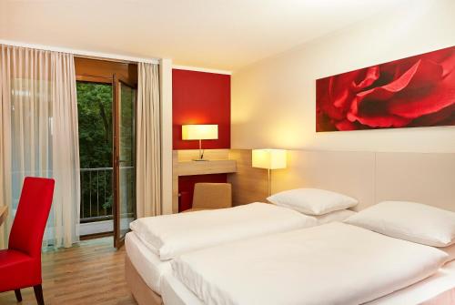 a hotel room with two beds and a red chair at H+ Hotel Bad Soden in Bad Soden am Taunus