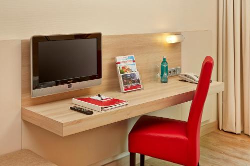 a room with a desk with a television and a red chair at H+ Hotel Bad Soden in Bad Soden am Taunus