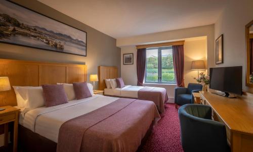 a hotel room with two beds and a desk and a television at Clifden Station House Hotel in Clifden