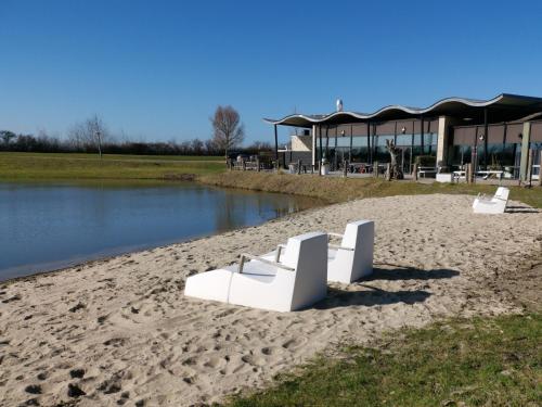two white benches sitting on the sand near a body of water at Resort Land & Zee in Scharendijke
