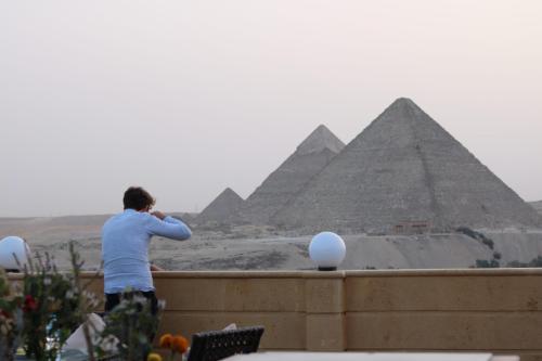um homem parado numa parede a olhar para as pirâmides em Gardenia Pyramids view inn no Cairo