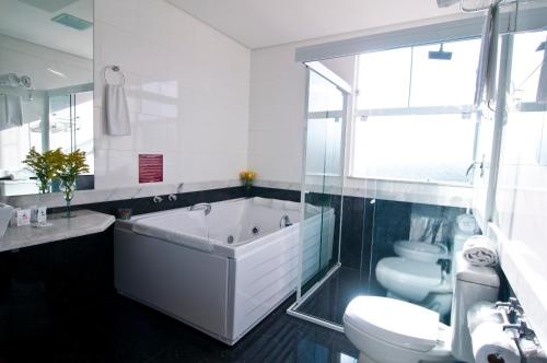 a bathroom with a tub and a toilet and a sink at Alfa Hotel in Viçosa