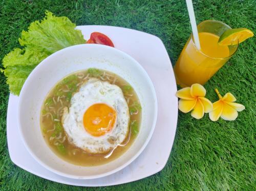 eine Schüssel Suppe mit einem Ei darin und einem Drink in der Unterkunft Pondok DenAyu Homestay in Kuta