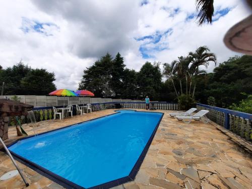 a blue swimming pool with chairs and umbrellas at Hospedagem Chalé pousada Chácara Cantinho do Mozão in São Roque