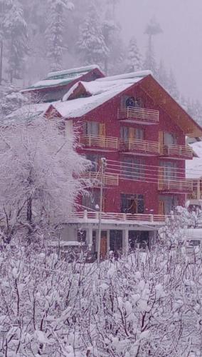 a large red building with snow on the roof at New Apple Cottage in Manāli
