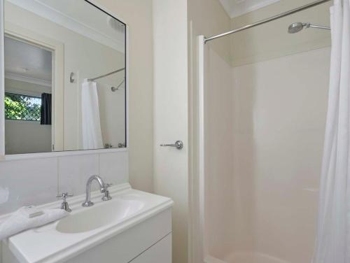 a white bathroom with a sink and a mirror at Queens Beach Tourist Village in Bowen