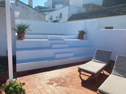 a patio with two chairs and a white wall at Alojamiento Armenia Piscina in Alcalá de los Gazules