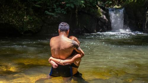 a man standing in the water in front of a waterfall at Pousada Salve Floresta in Tapiraí