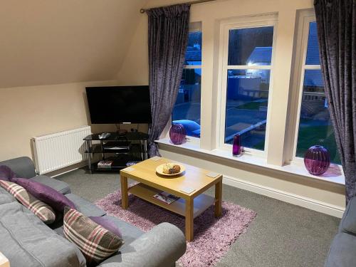 a living room with a couch and a table and windows at Balmaha Lodges and Apartments in Balmaha