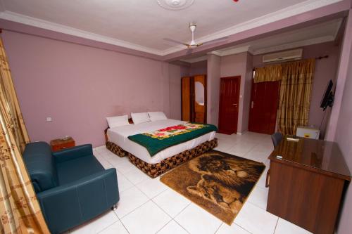 a bedroom with a bed and a blue couch and a television at Pemicsa Hotel Accra in Spintex