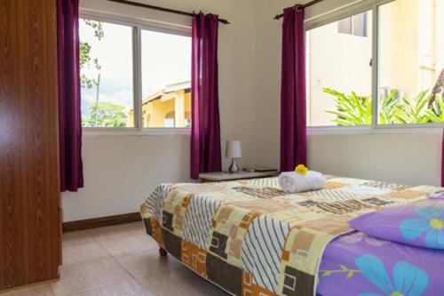 a bedroom with a bed with purple curtains and windows at Josies Cottage in Beau Vallon