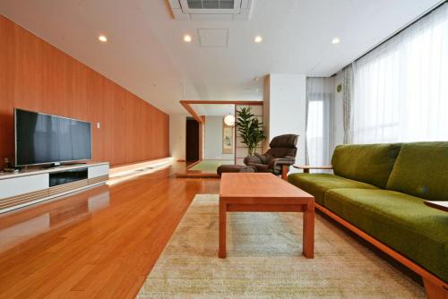 Hostel PLEASURE MARUYAMA في سابورو: غرفة معيشة مع أريكة خضراء وتلفزيون