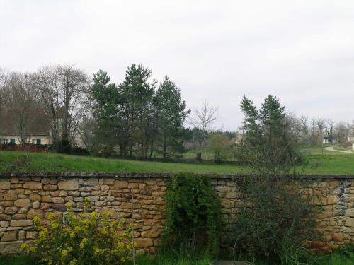 a stone wall with trees and a field behind it at La Grange aux Roses in Tursac