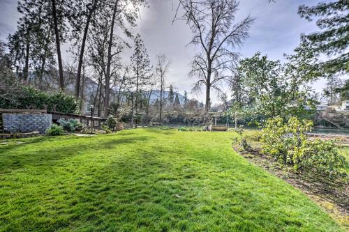 a yard with green grass and trees and a fence at Serene Riverfront Escape with Hot Tub and Views! in Grants Pass